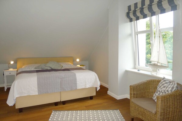A bedroom with a bed, a nightstand, a chair, a window with curtains, and a view of trees outside.