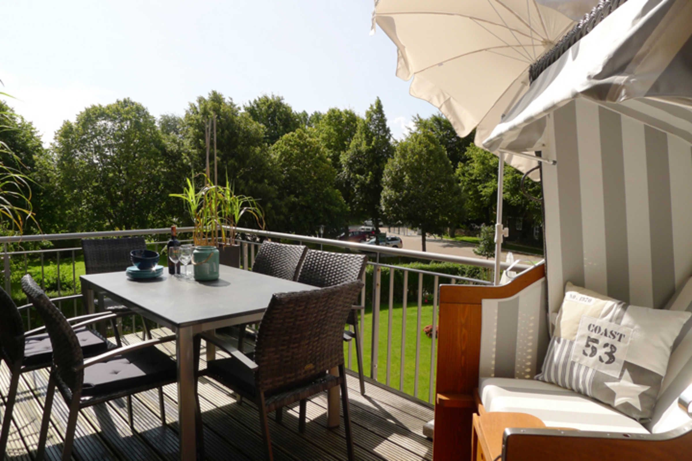 Une terrasse avec une table et des chaises, un coin salon avec des coussins, et une vue sur une pelouse verdoyante et des arbres.