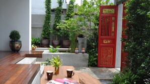 A wooden table with magazines and a plant, surrounded by potted plants and a red door with decorative elements. - Udee Bangkok (Bangkok)