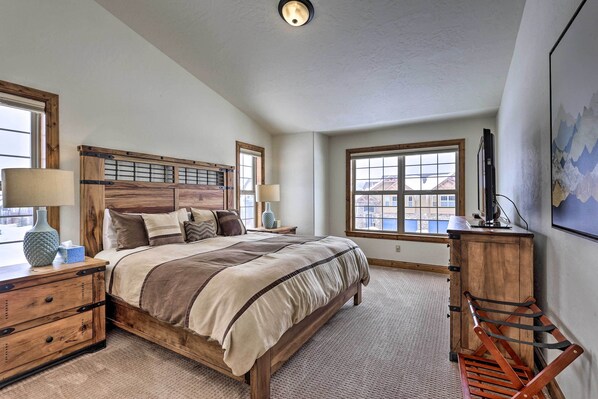 A bedroom with a wooden bed, two bedside tables, a nightstand, a chair, a TV, and a large window.