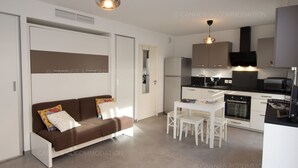 Une cuisine moderne avec des meubles blancs, une table à manger avec des chaises et un canapé marron agrémenté de coussins à motifs.