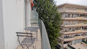 A balcony with a table and chairs, overlooking a building with multiple balconies and a large tree. - Montrachet-2429-Modern 2 bed rooms in the city center (Cannes)