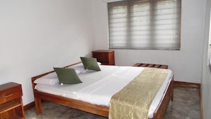 Una cama individual con estructura de madera, dos mesitas de noche, una ventana con persianas y una colcha color beige.