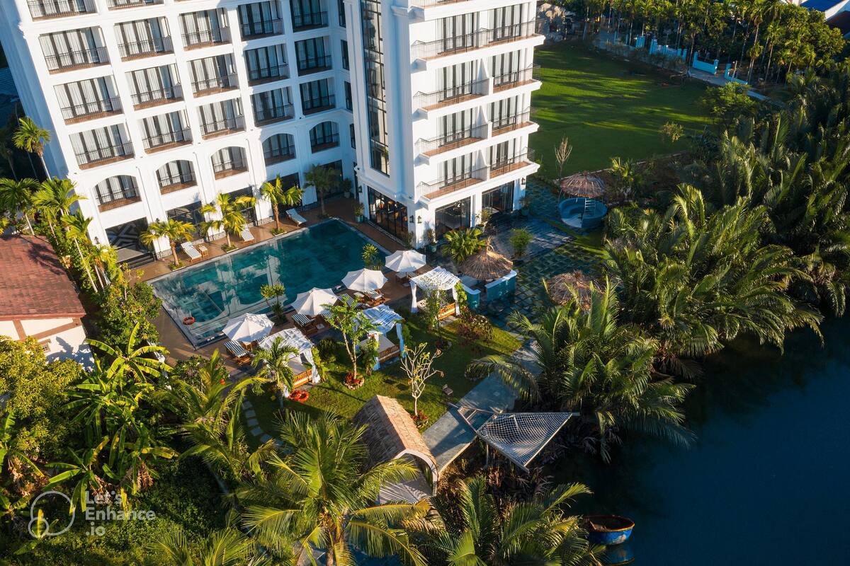 A high-rise hotel with multiple balconies, a swimming pool, and lush tropical landscaping.