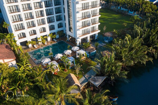 A high-rise hotel with multiple balconies, a swimming pool, and lush tropical landscaping. - Shining Riverside Hoi An Resort & Spa (Da Nang)
