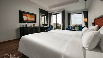 Habitación de hotel con una cama grande, un escritorio con silla, un televisor mostrando 'BREAKING NEWS' y un balcón con vistas.