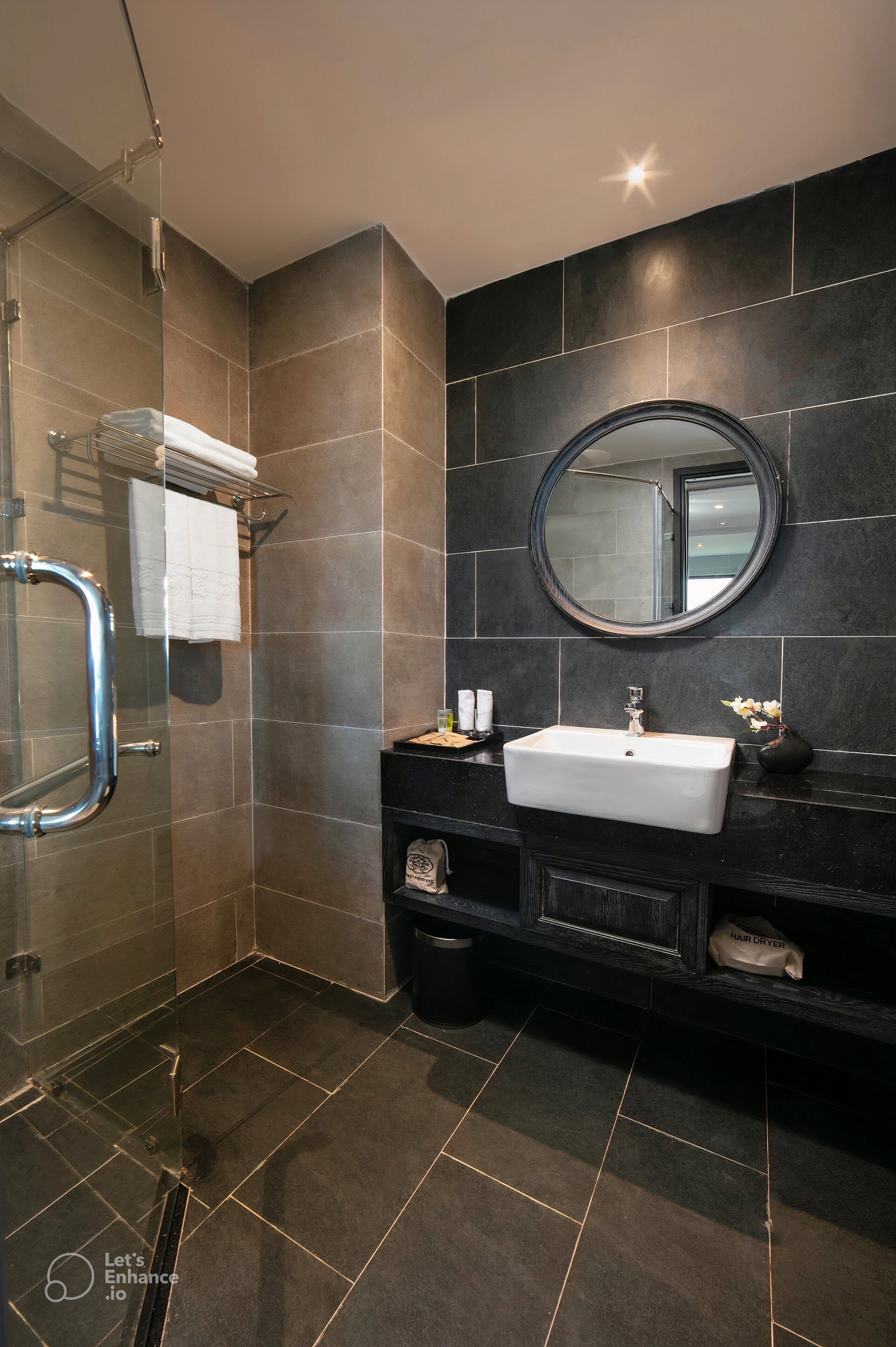 A modern bathroom with a glass-enclosed shower, a white sink, and a round mirror.