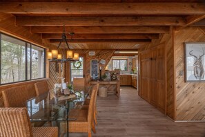 Un interno in legno con un tavolo da pranzo in vetro, sedie in vimini e un angolo cottura con pensili in legno.