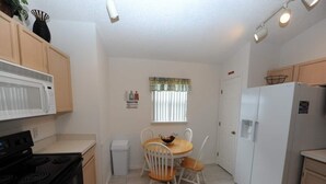 A compact kitchen with a stove, microwave, and refrigerator. There is a small dining table with chairs and a window with blinds. - Palmview Villa - your perfect retreat in Clermont by Paradise Resort Vacations! (Clermont)