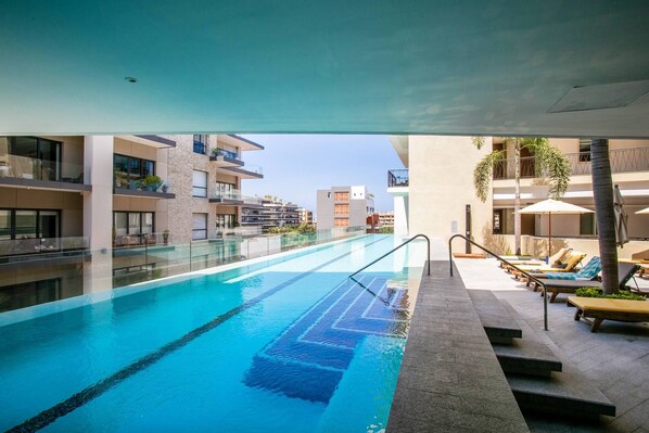 En pool med fri utsikt över de omgivande byggnaderna och ett avslappningsområde med solstolar.