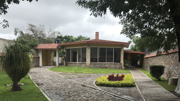 A house with a stone pathway leading to a front door, surrounded by a well-maintained lawn and a small garden. - Casa redonda a 15 min de la media luna (Ciudad Fernández)