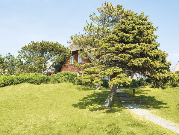 A traditional house with a thatched roof, surrounded by well-maintained lawns and a large tree. - Strandidyll by A&M - Strandidyll (Kampen (Sylt))