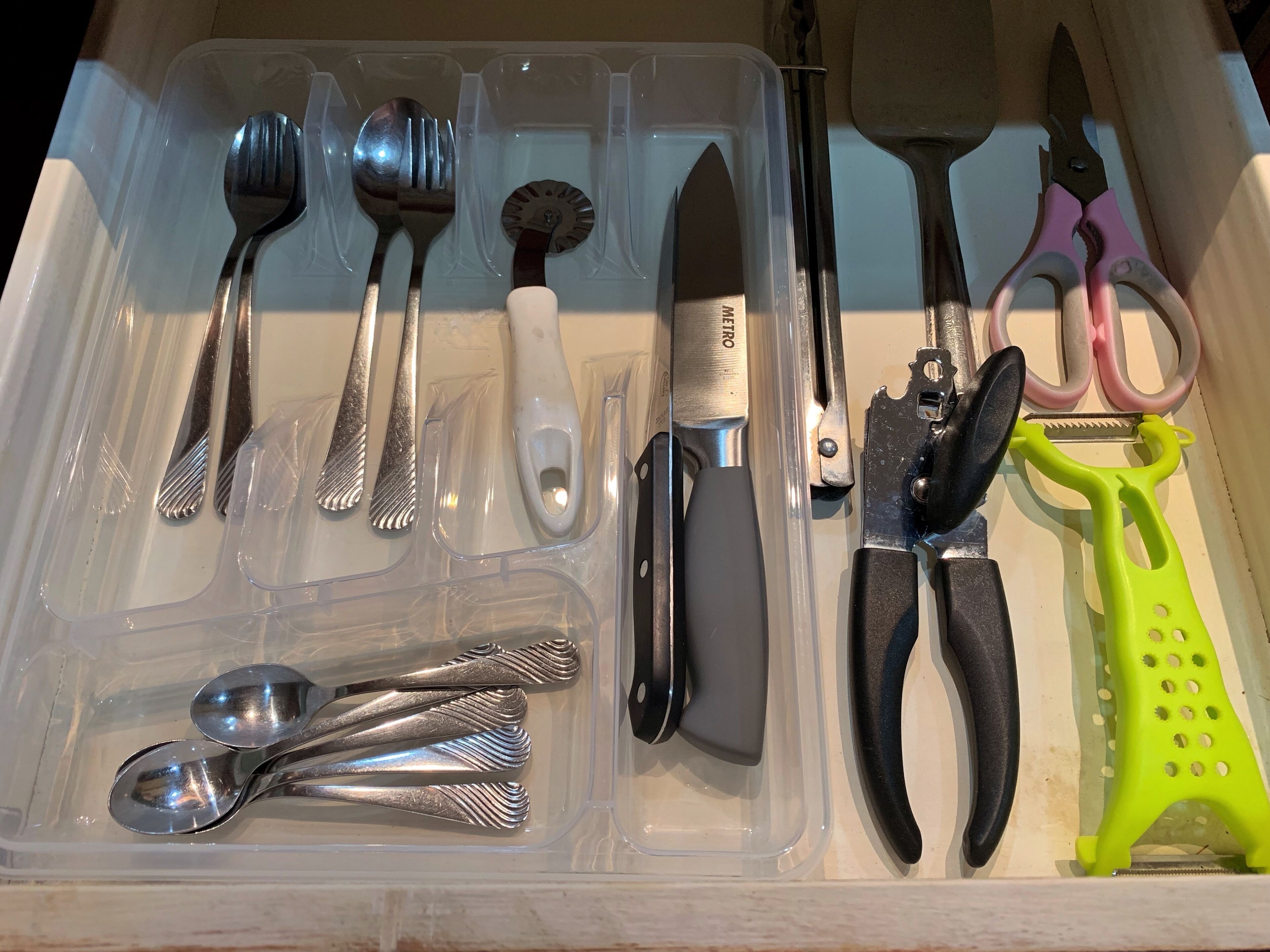 A drawer containing various kitchen utensils including spoons, a knife, and a grater.