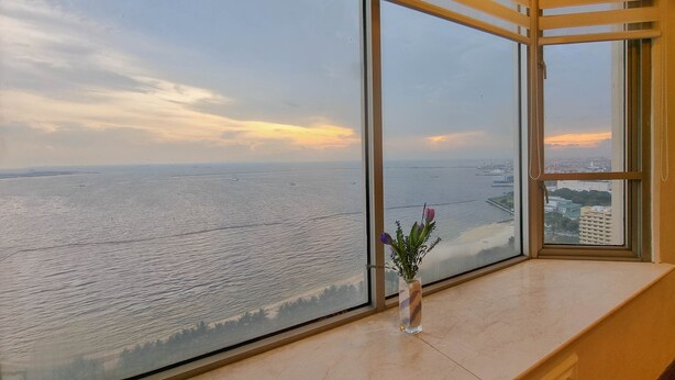 A room with large windows overlooking a body of water and a cityscape. - Marina Residential Suites (Manila)
