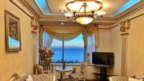 A luxurious room with ornate furniture, a chandelier, a television, and a view of the sea. - Marina Residential Suites (Manila)