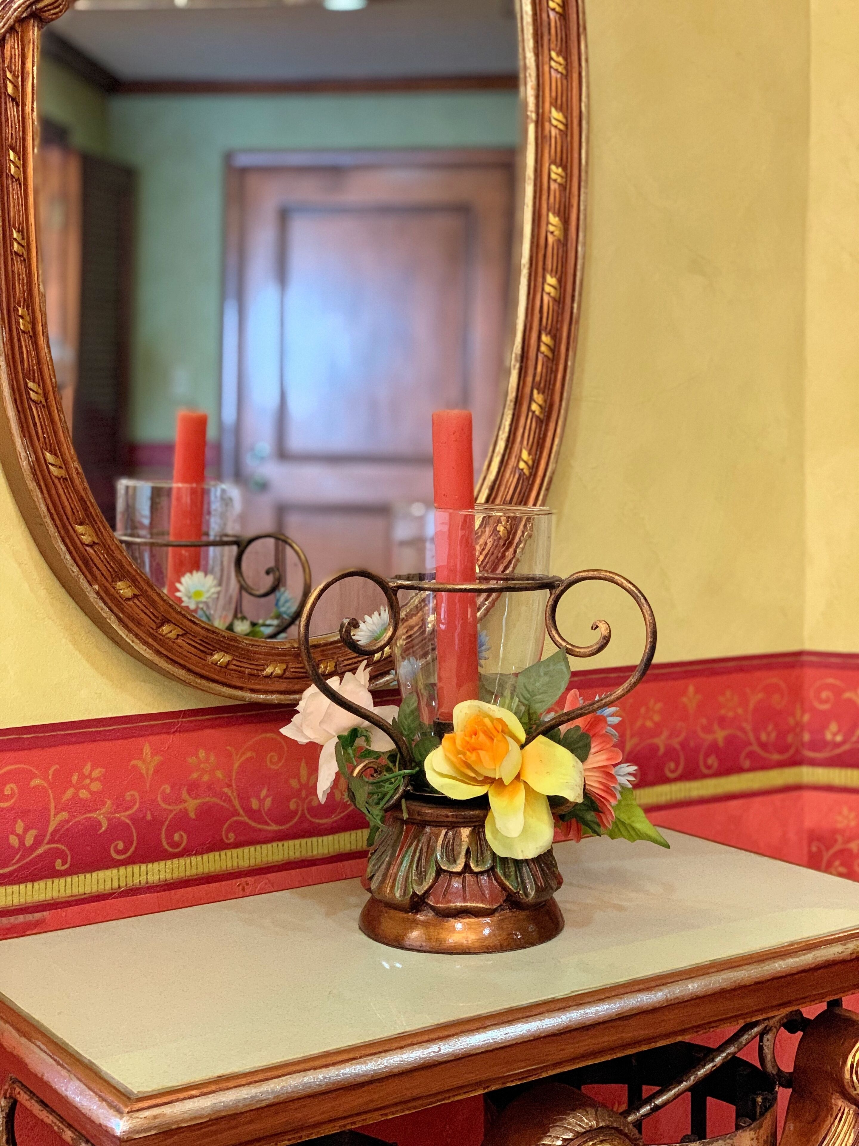 A mirror with a decorative frame, a vase with flowers, and a candle on a table.