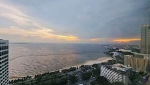 A coastal cityscape with a view of the sea, buildings, and a sunset. - Marina Residential Suites (Manila)