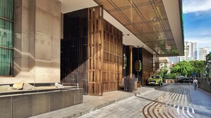 A modern building entrance with a stone facade, a wooden decorative screen, and a paved area with a unique pattern. - Marina Residential Suites (Manila)