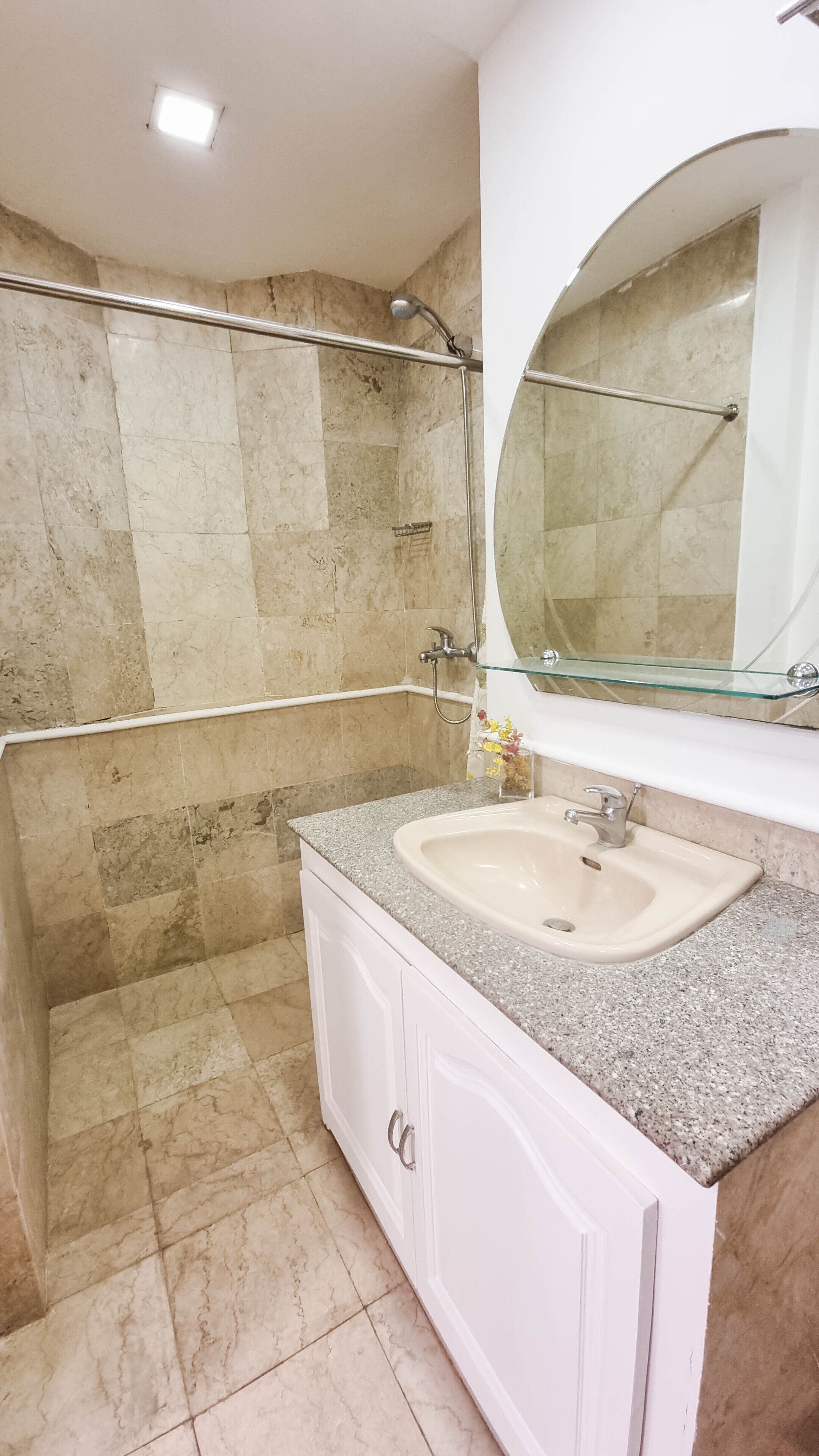 A bathroom with a granite countertop sink, a glass shower enclosure, and a white vanity.