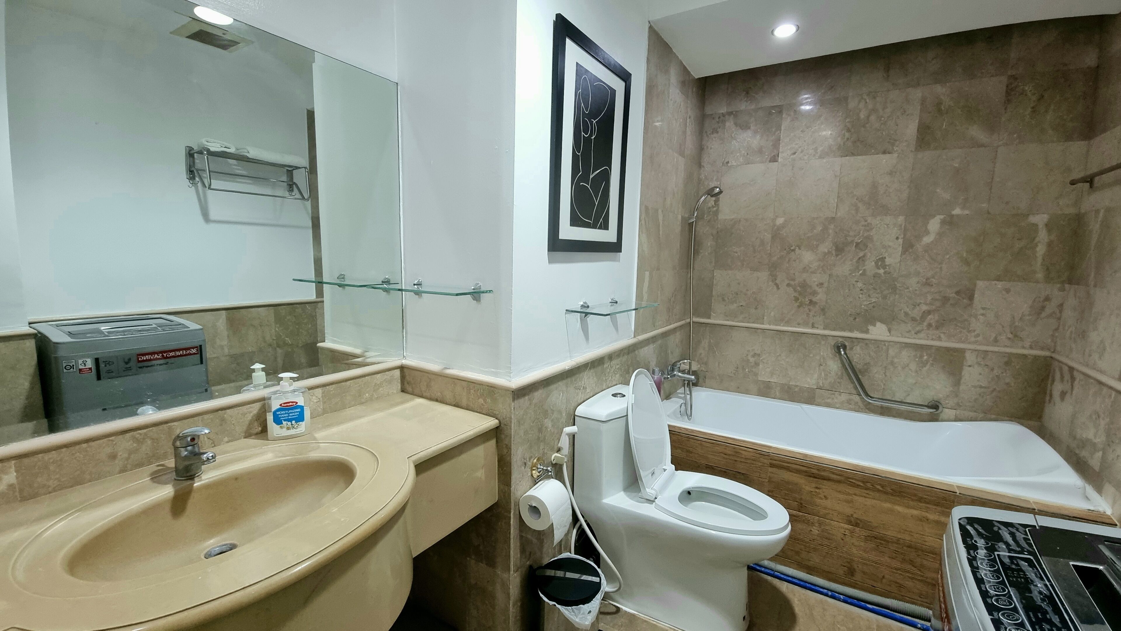 Un baño moderno con un lavamanos color beige, inodoro blanco y bañera. Cuenta con un box de ducha de vidrio, un perchero y un dispensador de gel antibacterial.