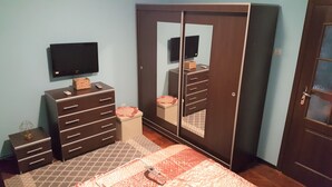 A bedroom with a wardrobe, a television, a small bedside table, and a bed with a patterned bedspread. - Venus Plaza Apartment (Ploiești)