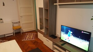 A living room with a flat-screen TV, a wooden coffee table, a yellow chair, and a patterned rug. - Venus Plaza Apartment (Ploiești)