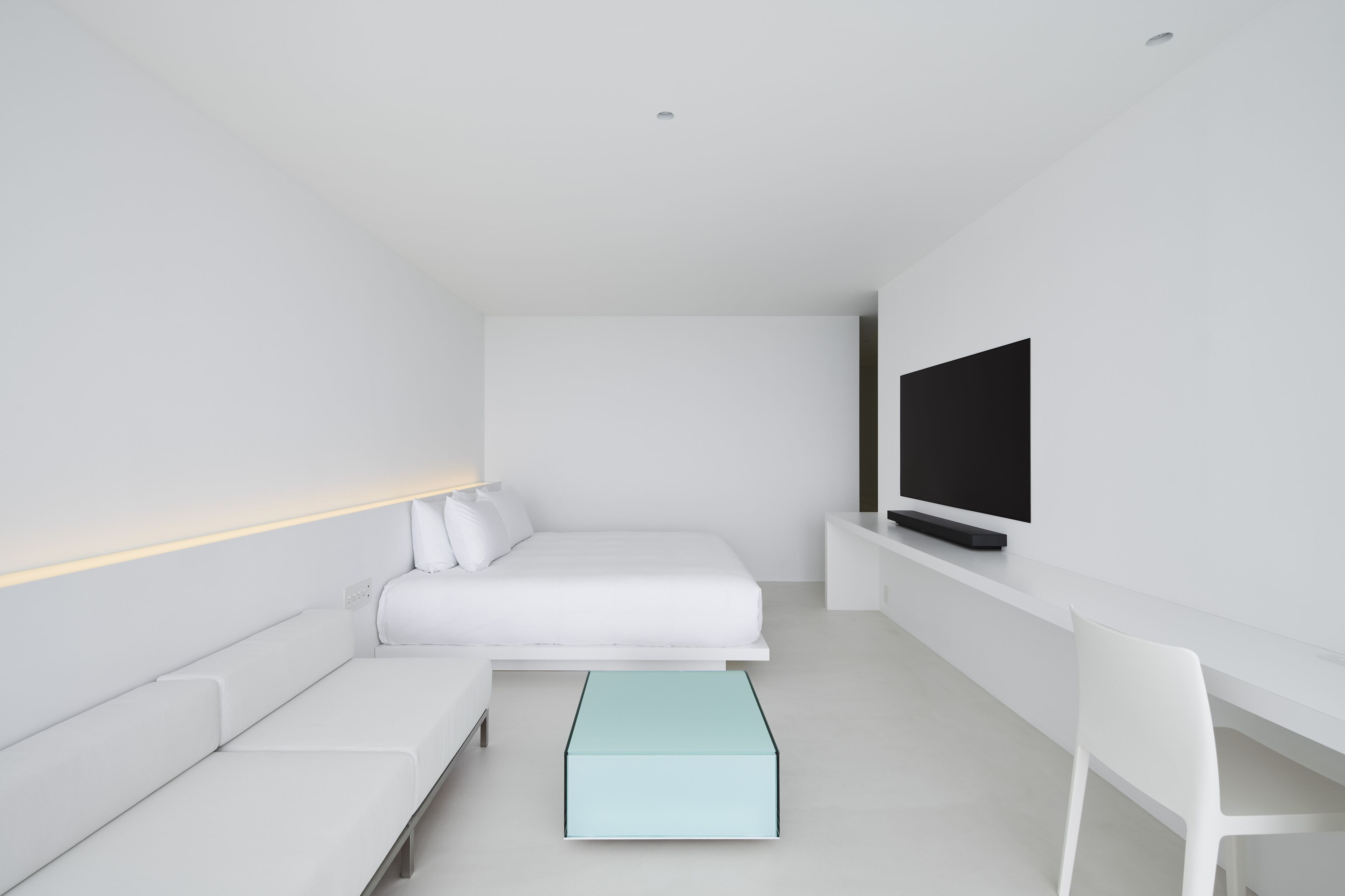 A modern, minimalist bedroom with a bed, a TV, a desk, and a chair.