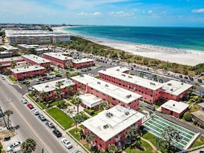 A coastal hotel area with multiple red-roofed buildings, a beach, and a clear view of the ocean.