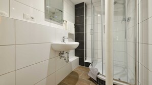 A modern bathroom with a white sink, a glass shower enclosure, and a dark accent wall.