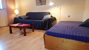 Una habitación pequeña y acogedora con un sofá, una cama individual, una mesa de madera y una lámpara.
