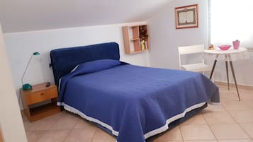 A bedroom with a bed, a desk, a chair, a lamp, a shelf with books, and a framed certificate on the wall.