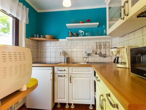 A compact kitchen with a teal wall, white cabinets, and a coffee maker. - Holiday house Schwalbennest (Ummanz)