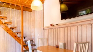 Un interior de madera con una mesa redonda y sillas, una escalera y un televisor fijado a la pared.