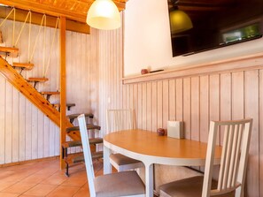 A wooden interior with a round table and chairs, a staircase, and a TV mounted on the wall.