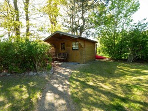 A small wooden cabin with a bench outside, surrounded by trees and grass. - Holiday house Schwalbennest (Ummanz)