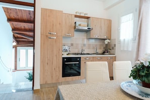 A modern kitchen with wooden cabinets, a built-in oven, and a dining area with white chairs and a table.