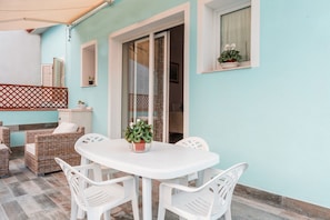 An outdoor patio with a white table and chairs, wicker furniture, and potted plants.
