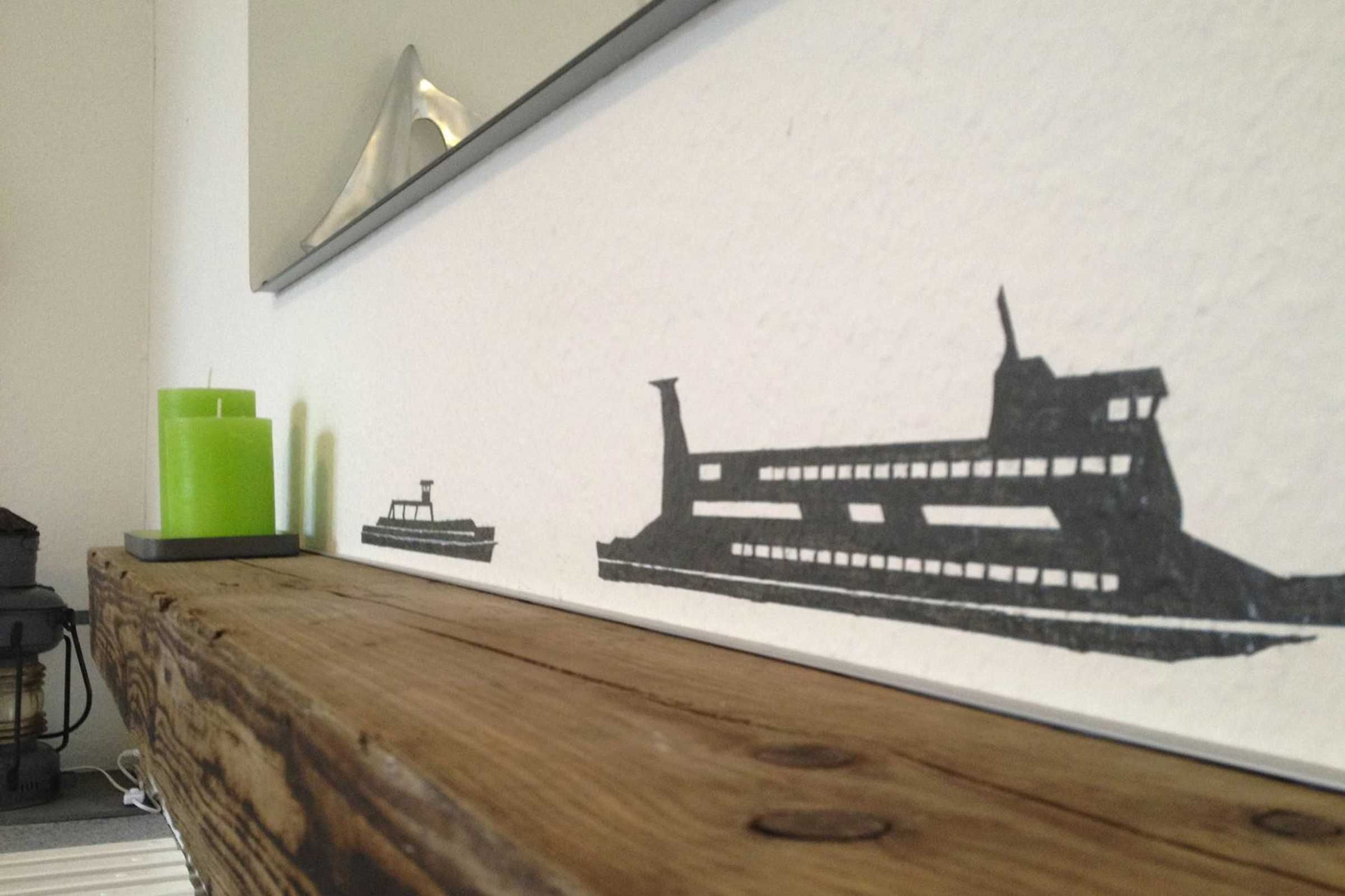 Een muur met een zwart-wit silhouet van een schip, een groene kaars en een klein bootmodel.