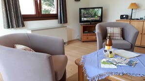 Een woonkamer met twee banken, een salontafel met folders, een televisie en een lamp.