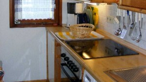 Een kleine keuken met houten kastjes, een raam met een geruit gordijn, een spoelbak en een fornuis.