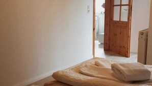 Un dormitorio con puerta de madera, una cama con manta color beige y pared blanca.