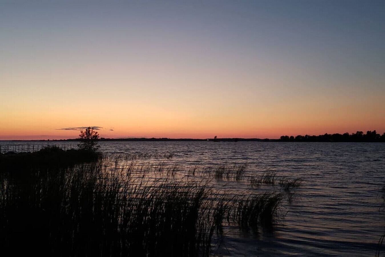 A calm body of water at sunset with a distant shoreline silhouette.