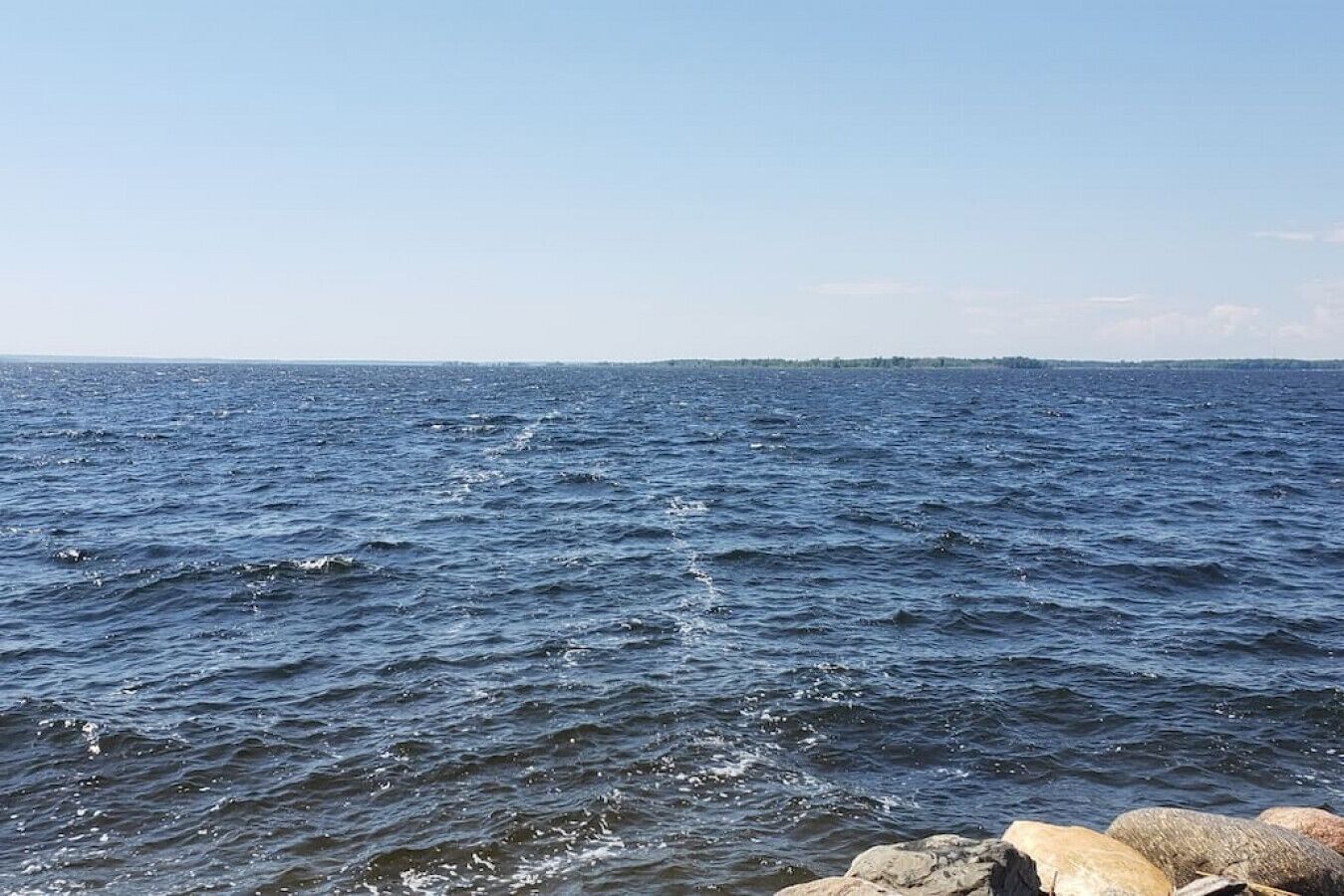 Une étendue d’eau avec des vagues, un ciel dégagé et une côte lointaine.