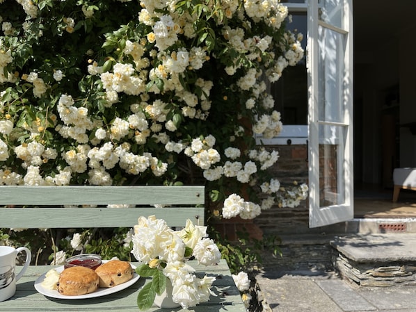 A table with pastries and a cup, set against a backdrop of white flowers and a wooden bench.