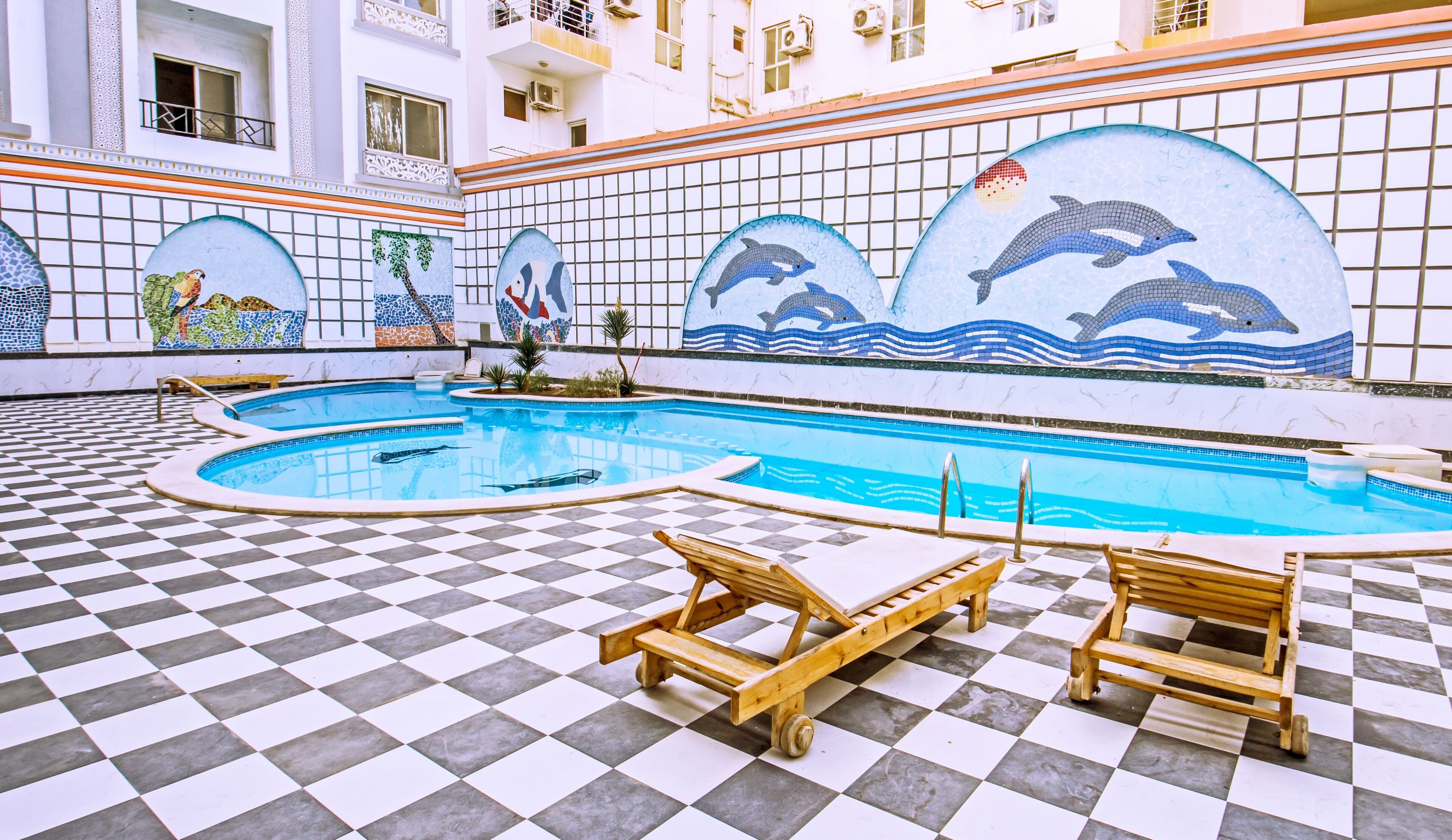A swimming pool with tiled walls and a checkered floor, surrounded by lounge chairs.