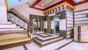 Un vaste hall d’entrée avec un sol en marbre, un escalier orné de rampes en métal ouvragé et un ascenseur moderne.