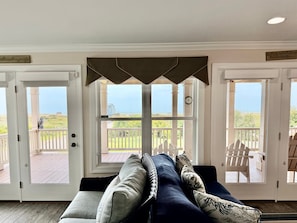 Une chambre avec vue sur la plage, une terrasse en bois et un canapé agrémenté de coussins.