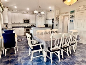 Een keuken met witte kasten, een centraal eiland en een eethoek met witte stoelen en een geruit tafelkleed.