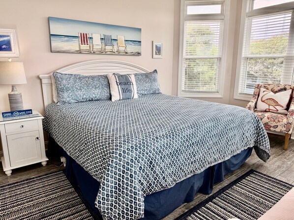 Een slaapkamer met een bed, nachtkastje, lamp, stoel en raam.