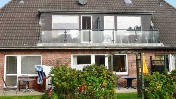Una casa de dos plantas con fachada de ladrillo, ventanas grandes y un balcón.
